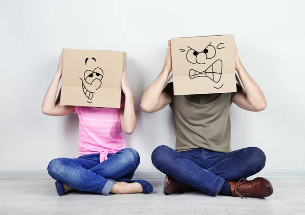 Couple with cardboard boxes on their heads sitting on floor near wall — Stock Photo, Image