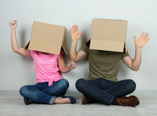 Couple with cardboard boxes on their heads sitting on floor near wall — Stock Photo, Image