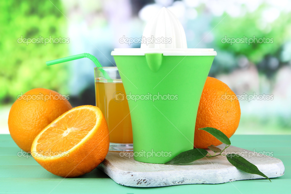 Citrus press, glass of juice and ripe oranges on green wooden table