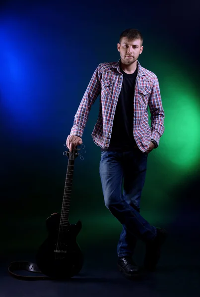 Young musician with guitar on dark color background — Stock Photo, Image