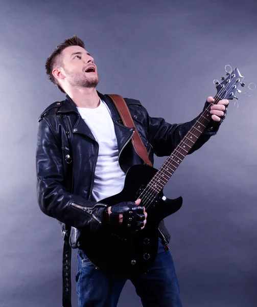 Junger Musiker, der Gitarre spielt und singt, auf dunklem Hintergrund — Stockfoto