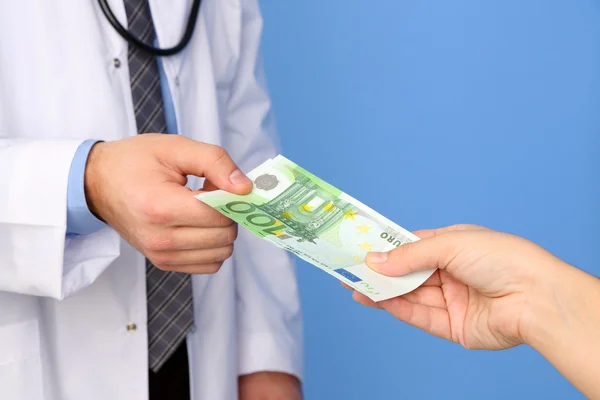 Médico masculino recebendo dinheiro do paciente, em fundo azul — Fotografia de Stock