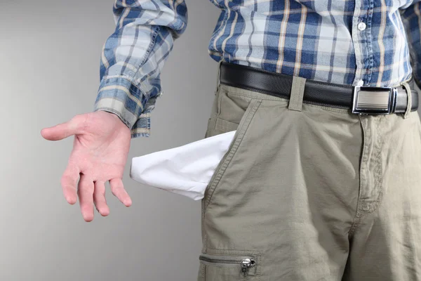 Hombre mostrando su bolsillo vacío sobre fondo gris —  Fotos de Stock