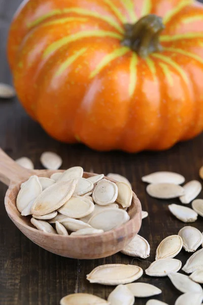 Pumpkin seeds in spoon with pumpkin on wooden background — Stock Photo, Image