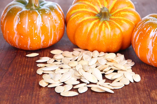 Pumpkin seeds with pumpkins on wooden background — Stock Photo, Image