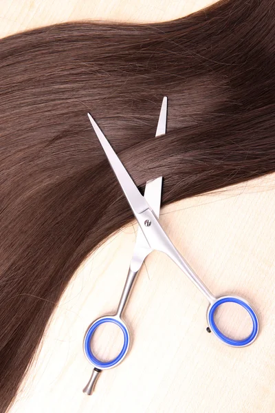 Cabelo castanho longo e tesoura em fundo de madeira — Fotografia de Stock