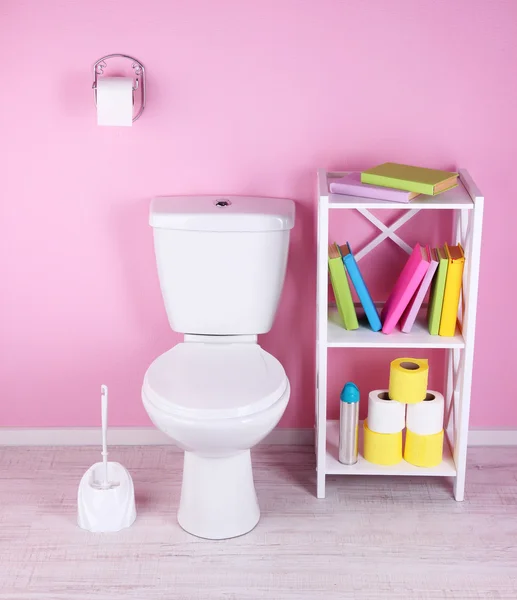 Weiße Toilettenschüssel und Ständer mit Büchern, auf farbigem Wandhintergrund — Stockfoto