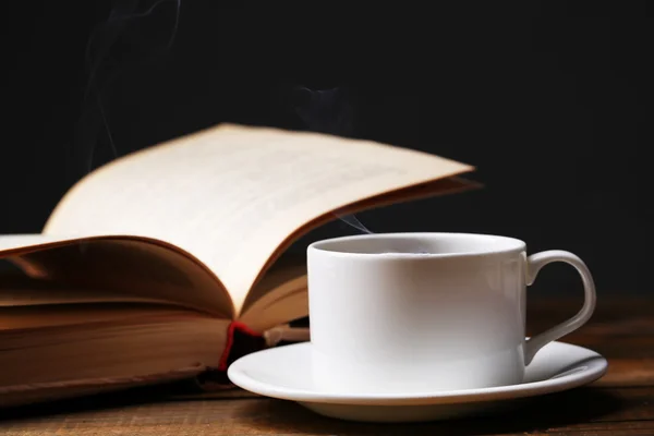 Kop warme koffie met boek op tafel op donkere achtergrond — Stockfoto