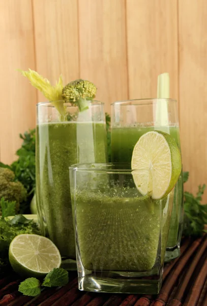 Bicchieri di succo di verdura verde e verdure su tappetino di bambù su sfondo di legno — Foto Stock