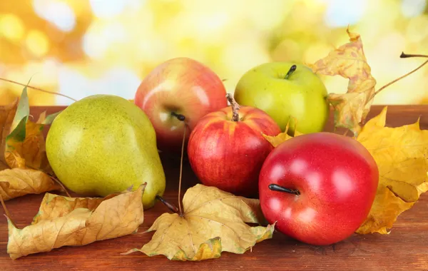 Vackra mogna äpplen och päron med gula blad på bordet på ljus bakgrund — Stockfoto