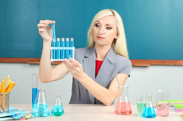 Chemielehrer mit Röhren am Tisch auf Tafel-Hintergrund — Stockfoto