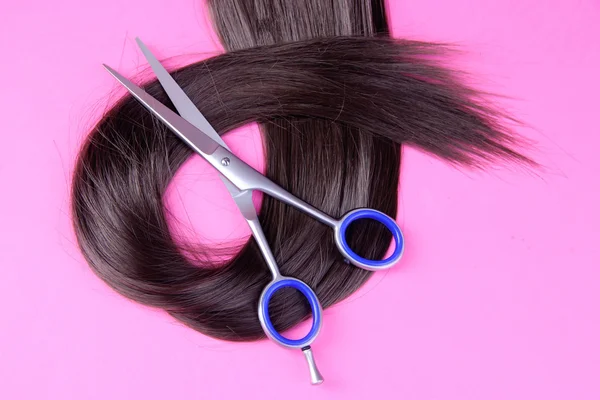 Long brown hair with scissors on pink background — Stock Photo, Image