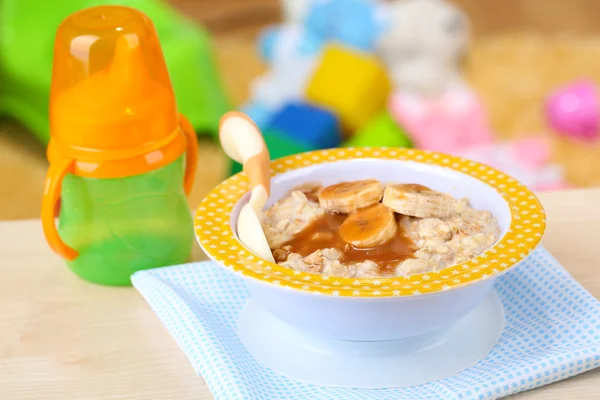 Tigela de mingau de cereal para bebê e brinquedos na mesa, no fundo de brinquedos — Fotografia de Stock