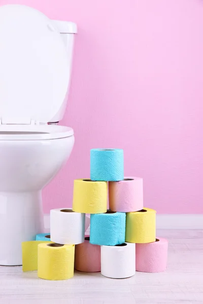 White toilet bowl and colorful rolls of toilet paper, in bathroom — Stock Photo, Image