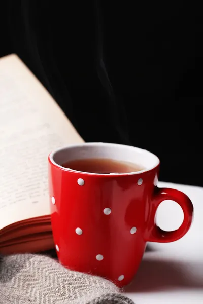 Taza de té caliente con libro y cuadros en la mesa sobre fondo oscuro — Foto de Stock