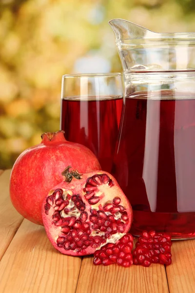 Vaso lleno y jarra de jugo de granada y granada en mesa de madera al aire libre — Foto de Stock