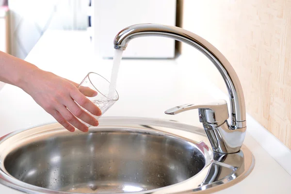 Vidrio de mano de agua vertido desde el grifo de la cocina — Foto de Stock