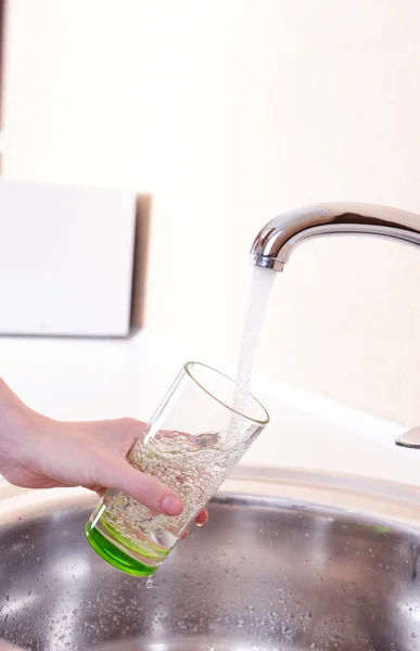 Hand holding glass of water poured from kitchen faucet — Stock Photo, Image