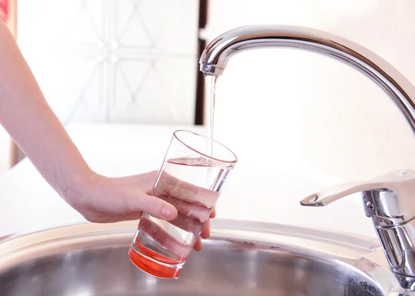 Hand holding glass of water poured from kitchen faucet — Stock Photo, Image