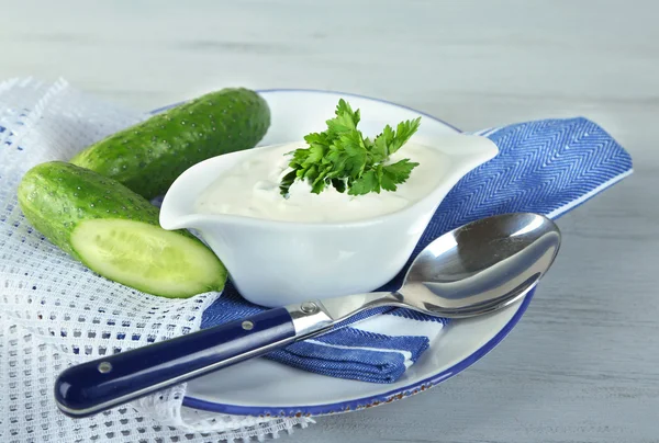 Komkommer yoghurt in sauceboat, op kleur servet, oncolor houten achtergrond — Stockfoto