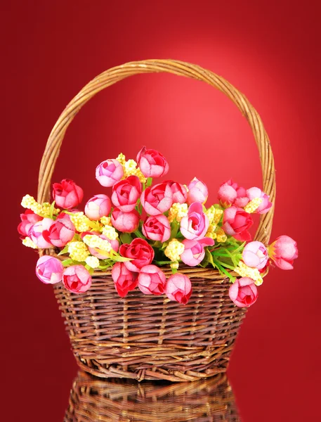 Bouquet of beautiful artificial flowers in wicker basket, on red background — Stock Photo, Image