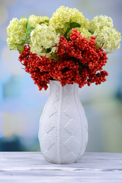 Blommor och bär i vas, på träbord, på ljus bakgrund — Stockfoto
