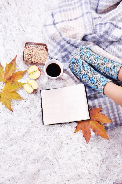 Composition with warm plaid, book, cup of hot drink and female legs, on color carpet background — Stock Photo, Image