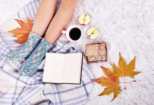 Samenstelling met warme plaid, boek, kopje warme drank te nemen en vrouwelijke benen, op een tapijt achtergrond kleur — Stockfoto
