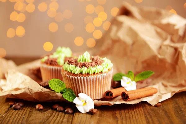 Cupcakes saborosos com creme de manteiga, na mesa de madeira, no fundo luzes — Fotografia de Stock