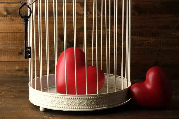 Hearts in decorative cage on wooden background — Stock Photo, Image