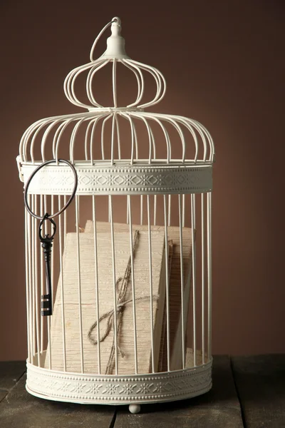 Books in decorative cage on wooden table, brown on background — Stock Photo, Image