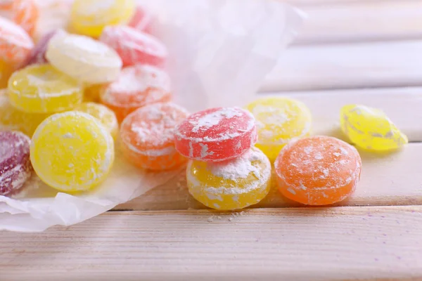 Sweet multicolor candies on paper, on color wooden background — Stock Photo, Image