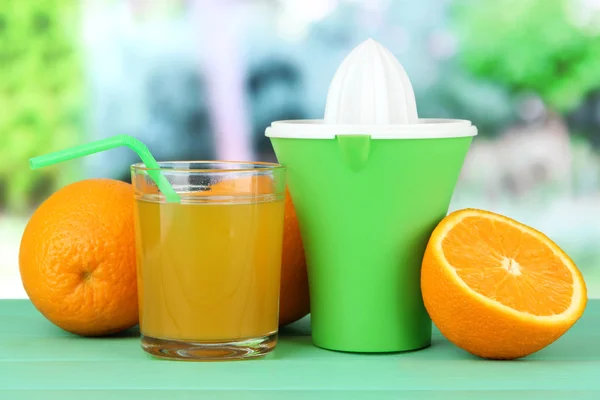 Citrus press, glass of juice and ripe oranges on green wooden table — Stock Photo, Image