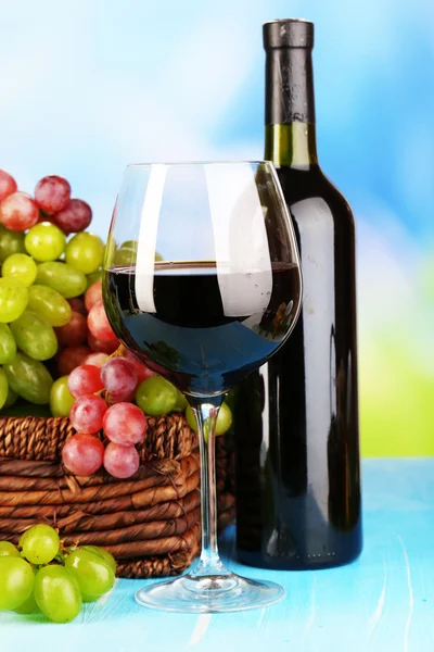 Ripe green and purple grapes in basket with wine on wooden table on natural background — Stock Photo, Image