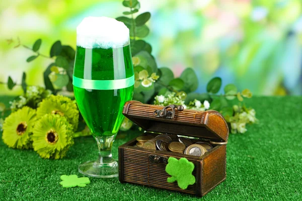 Glass of green beer and pitcher with coins on grass close-up — Stock Photo, Image