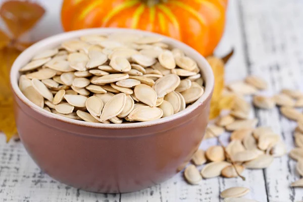 Semi di zucca in ciotola con zucca su fondo di legno — Foto Stock