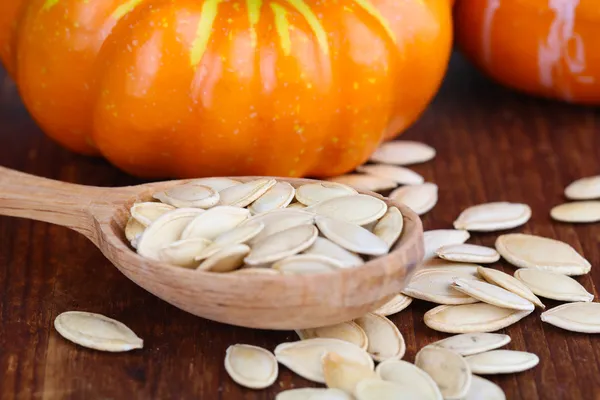 Semi di zucca in cucchiaio con zucche su sfondo di legno — Foto Stock