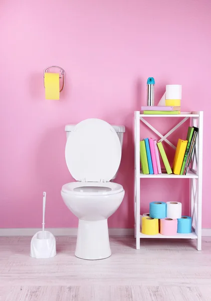 Tazón de inodoro blanco y soporte con libros, sobre fondo de pared de color — Foto de Stock