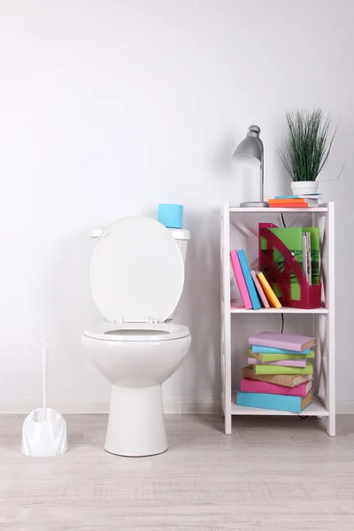 Vit WC-skål och stå med böcker, på färg vägg bakgrund — Stockfoto