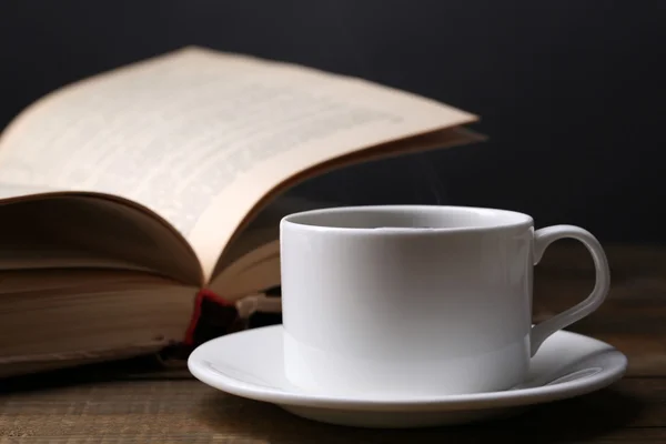 Taza de café caliente con libro en la mesa sobre fondo oscuro — Foto de Stock