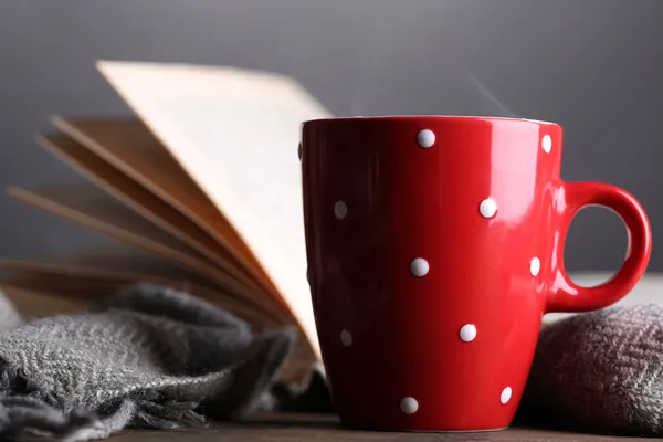 Cup of hot tea with book and plaid on table on gray background — Stock Photo, Image