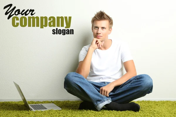Young man relaxing on carpet with laptop, on gray wall background — Stock Photo, Image