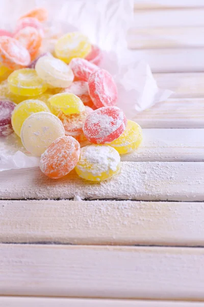 Сладкие разноцветные конфеты на бумаге, на цветном деревянном фоне — стоковое фото