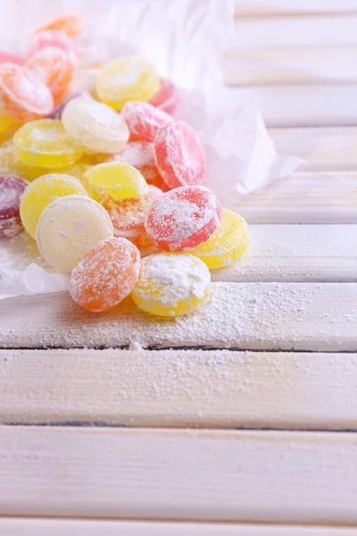 Sweet multicolor candies on paper, on color wooden background — Stock Photo, Image