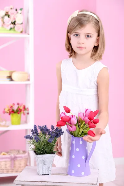 Beautiful little girl and stand with flowers on pink background — Stock Photo, Image