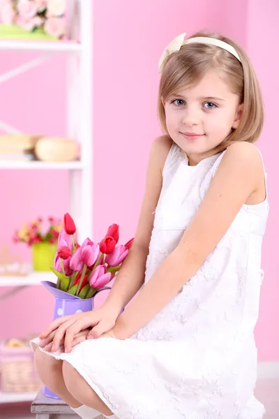 Little girl sitting on small ladder with flowers on pink background — Stock Photo, Image