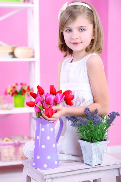 Little girl sitting on small ladder with flowers on pink background — Stock Photo, Image