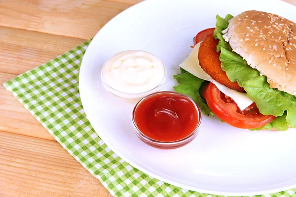 Sándwich sabroso con chuleta, sobre plato de color, sobre servilleta, sobre fondo de madera — Foto de Stock