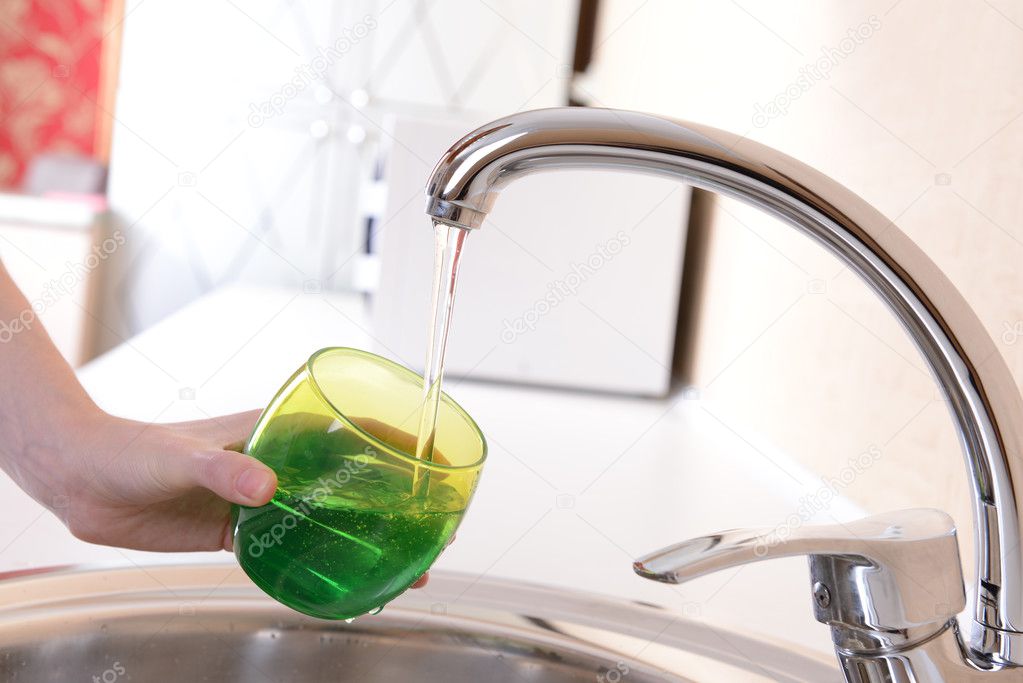 Hand holding glass of water poured from kitchen faucet