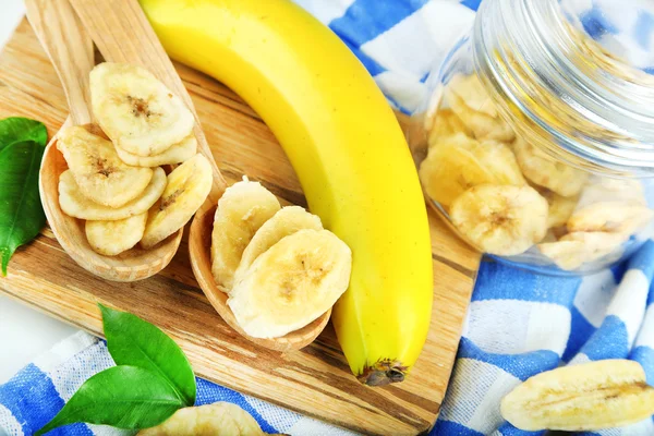 Frische und getrocknete Bananenscheiben im Glas, auf Schneidebrett, Nahaufnahme — Stockfoto